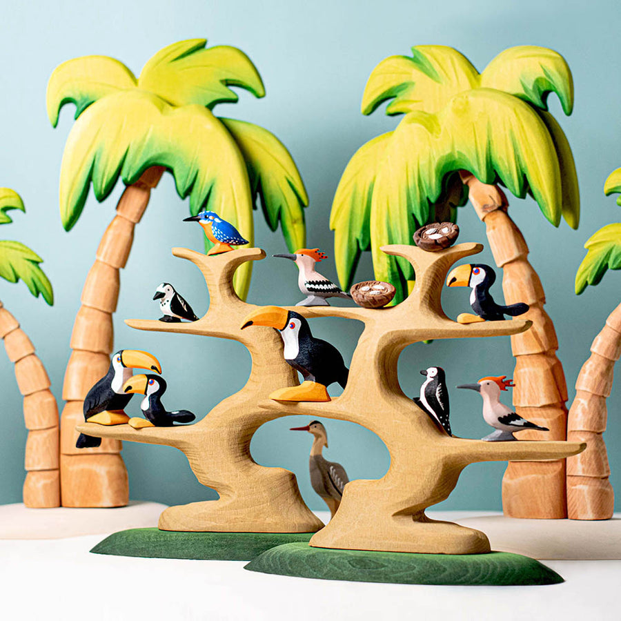 Bumbu wooden bird toy figures balanced on branches of the Bumbu Waldorf bird tree toys in front of some toy palm trees and a blue background