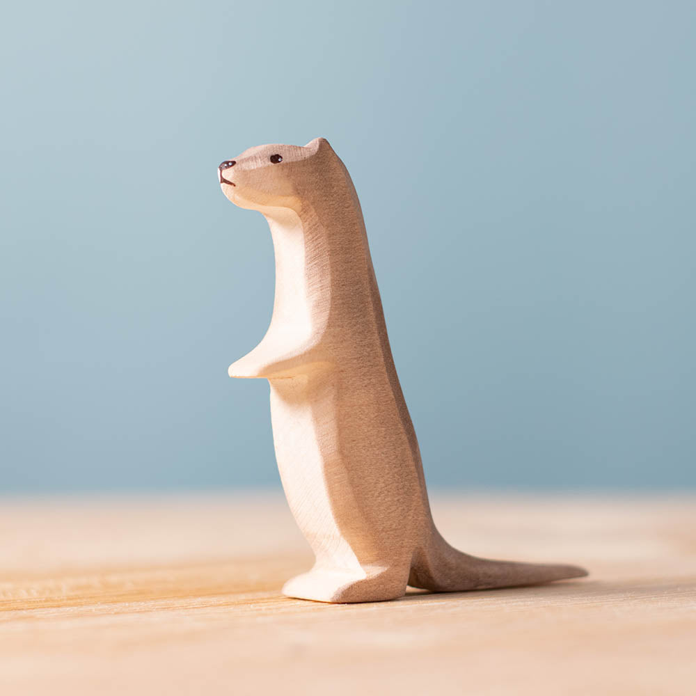 Close up of the Bumbu plastic-free wooden curious otter toy figure stood on a wooden surface in front of a blue background