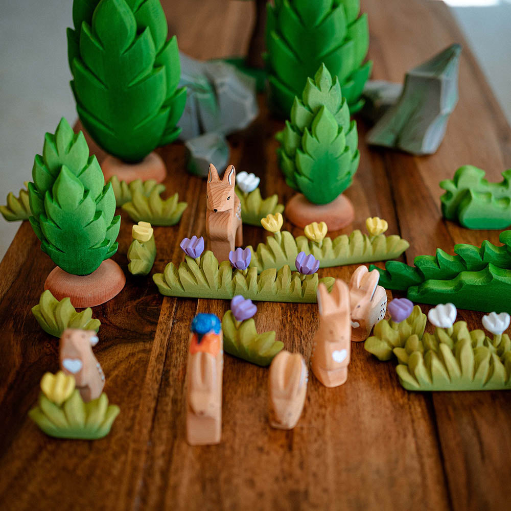 Bumbu hand carved wooden grass toys on a wooden table next to some Bumbu rabbit toys and wooden trees