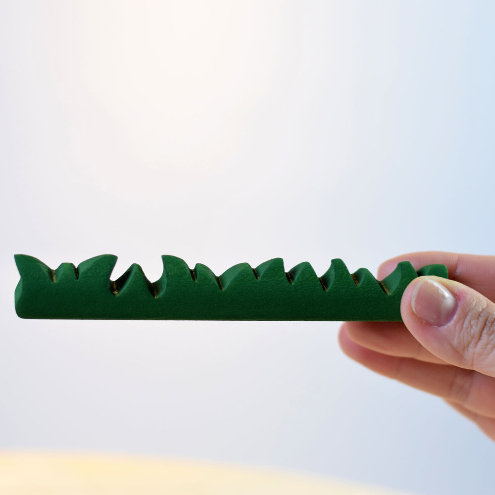 Close up of a hand holding the Bumbu plastic free wooden grass toy on a white background