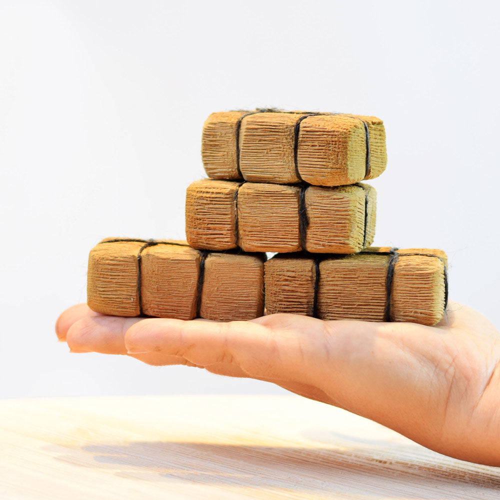 Close up of a hand holding the Bumbu plastic free wooden haystack blocks in front of a white background