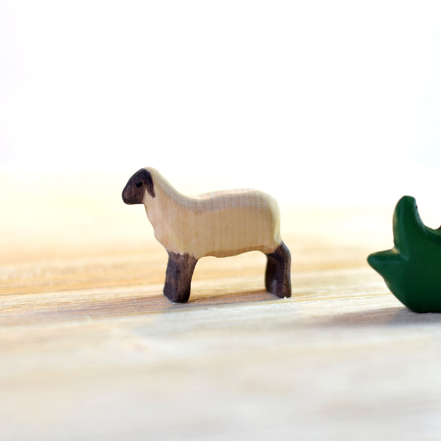 Bumbu kids small running lamb toy figure stood on a light wooden background next to a piece of bumbu wooden grass