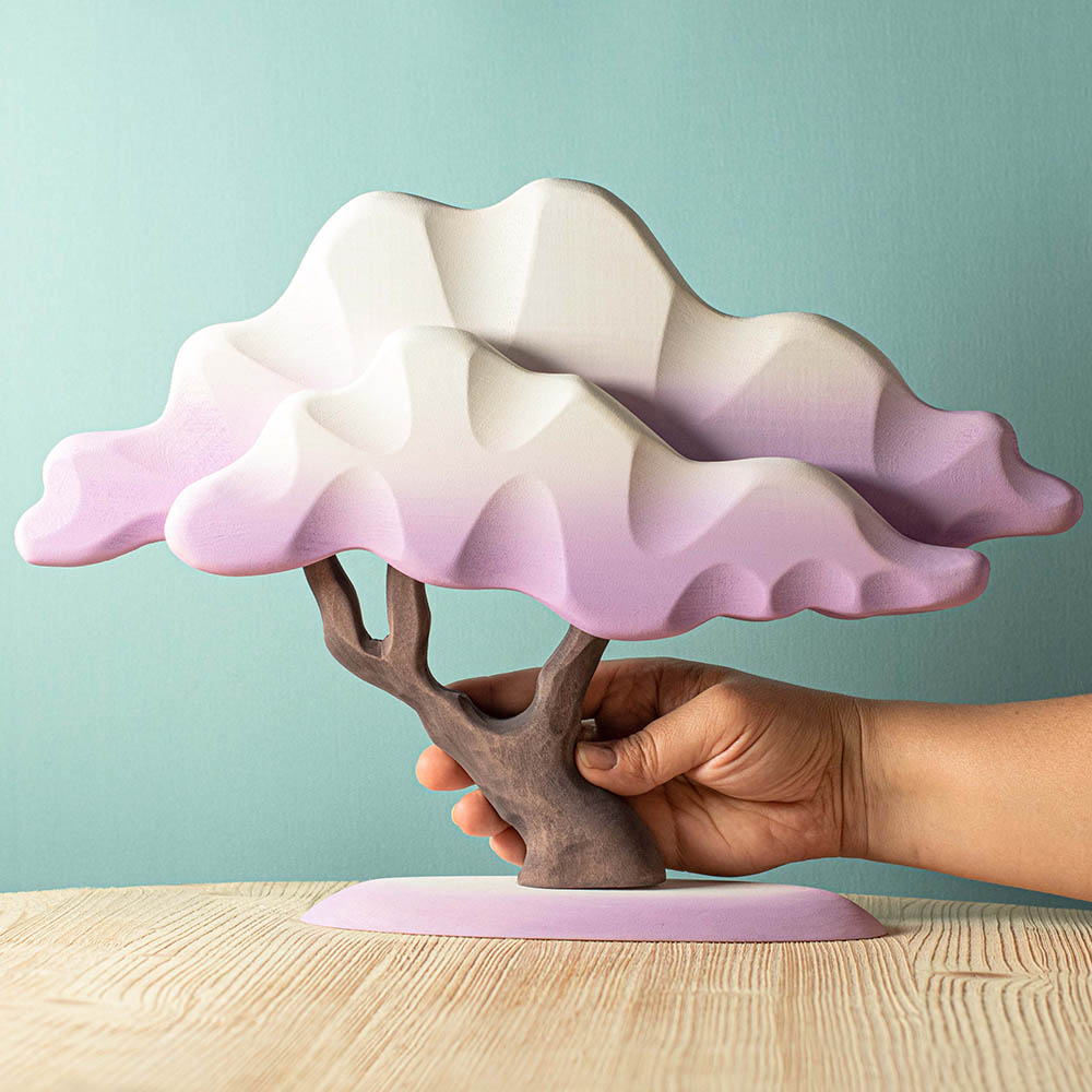 Close up of a hand holding the Bumbu lila winter Japanese maple tree toy on a wooden table