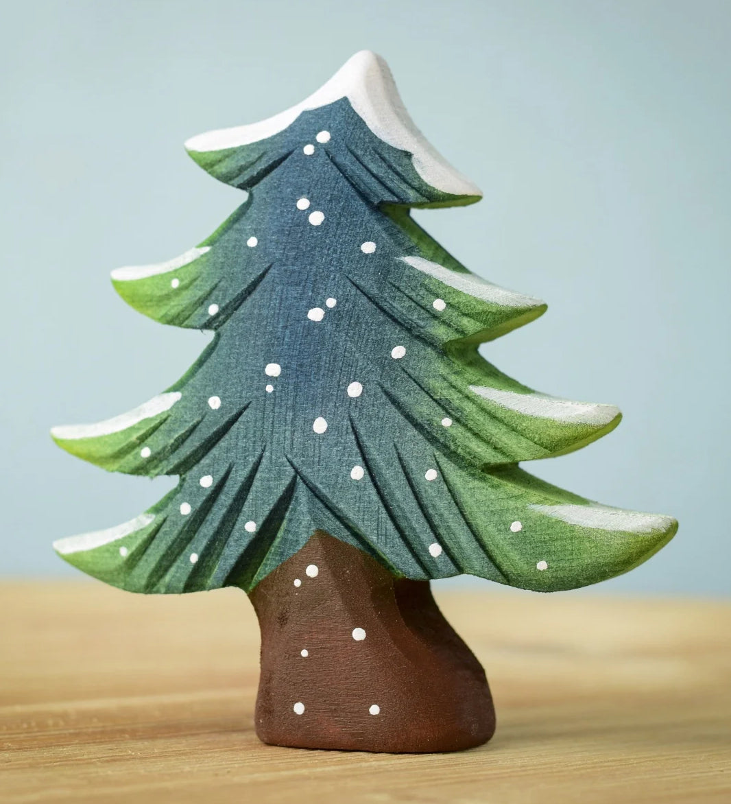 A Bumbu Small Snowy Fir Tree placed on a wooden surface.