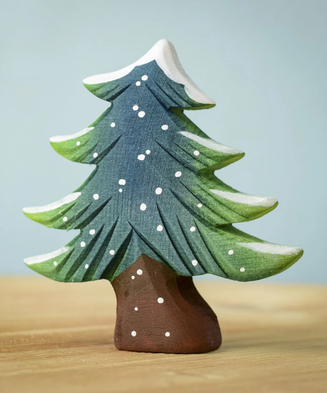 A Bumbu Small Snowy Fir Tree placed on a wooden surface.