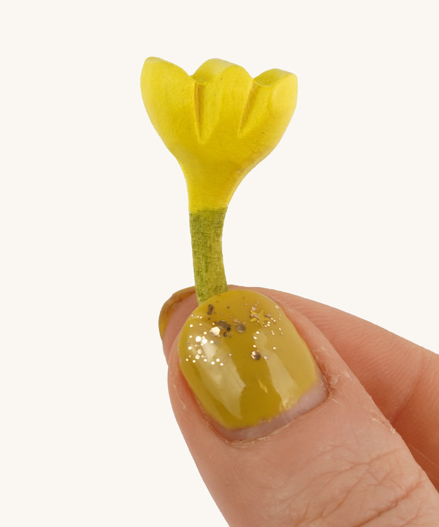 Bumbu Small Wooden Flower in Yellow bing held up in front of a cream background