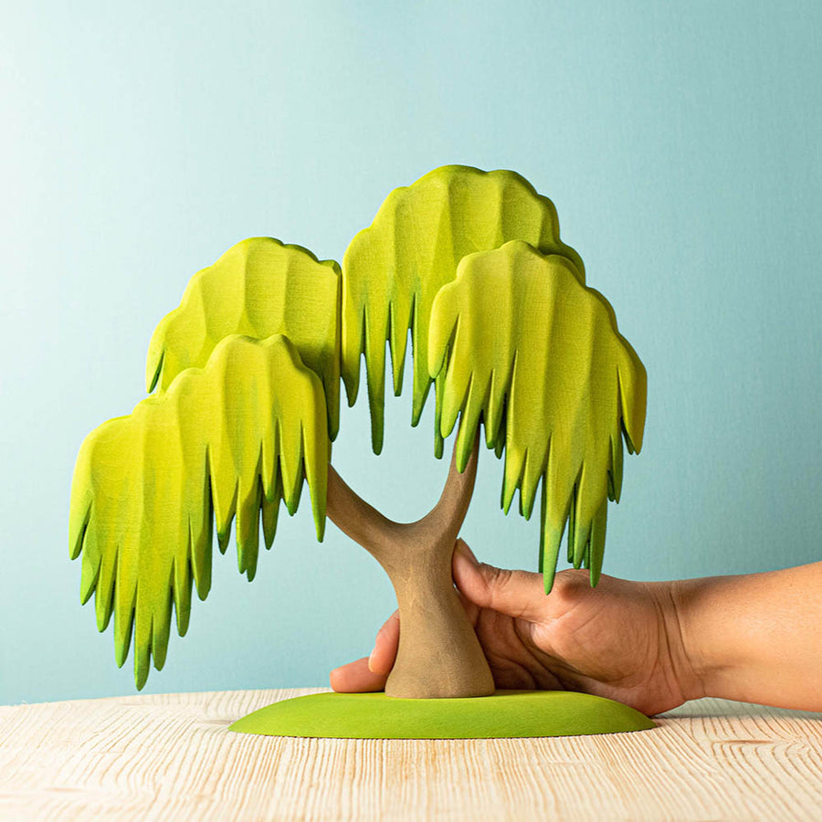 Close up of a hand holding a Bumbu handmade wooden Willow tree toy figure on a wooden worktop