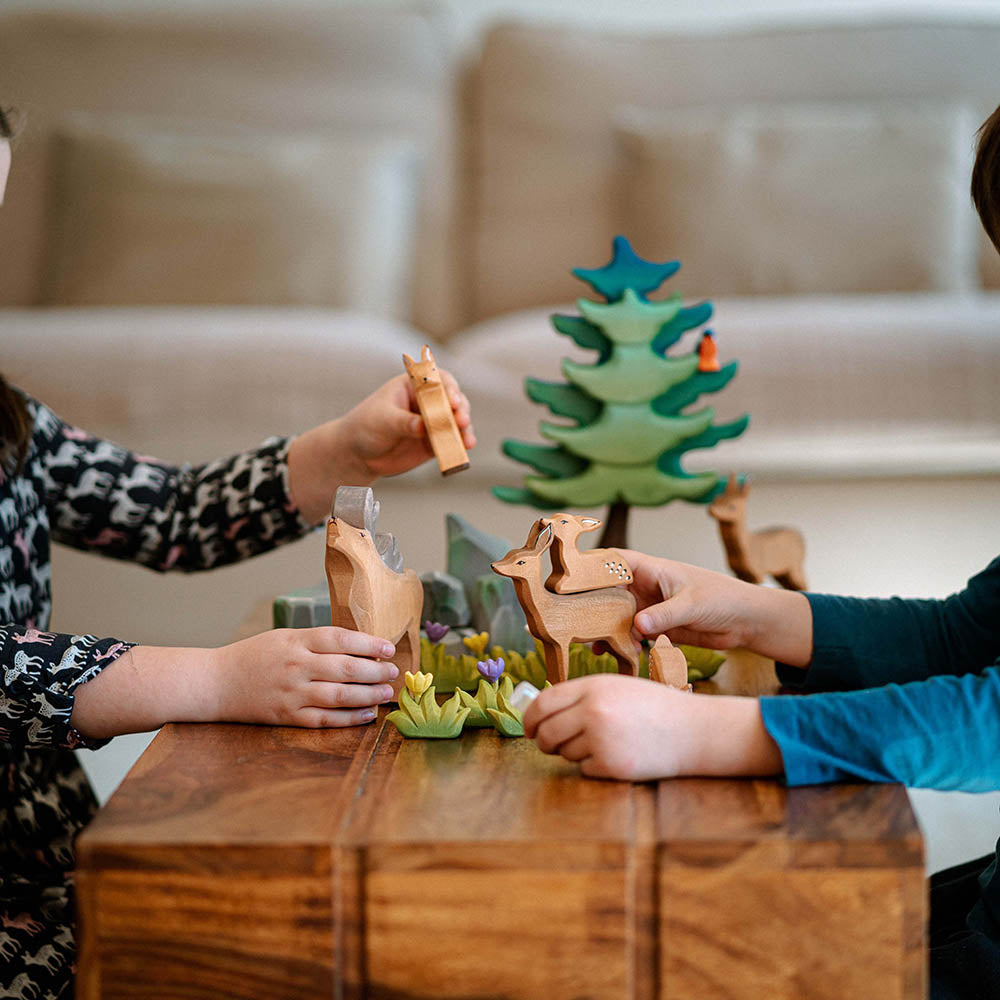 Close up of a childs hands holding the Bumbu plastic-free wooden deer toy next to a wooden otter figure