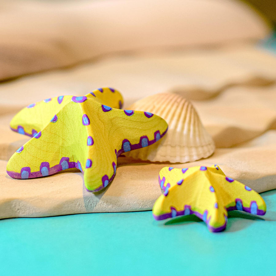 Bumbu wooden Yellow Starfish Set posed in a tropical beach scene with the Bumbu Red Starfish Set and Dolphin toys.