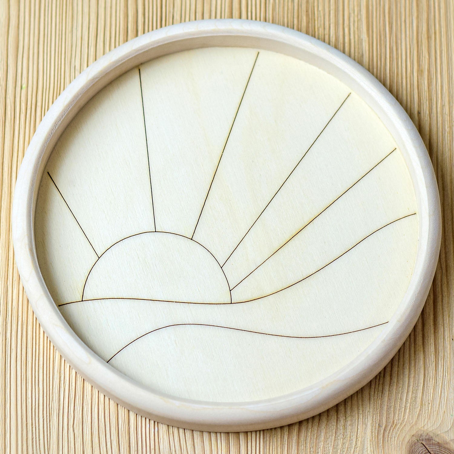 Circular wooden toy depicting the sun setting over the sea. A hand is in the photo showing the last piece being fitted to complete the scene.