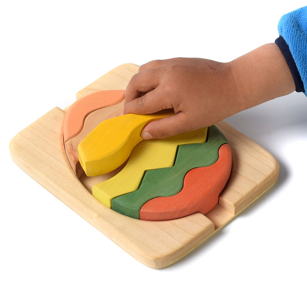 Hand placing the slotting wooden Bumbu egg  puzzle pieces together on a white background