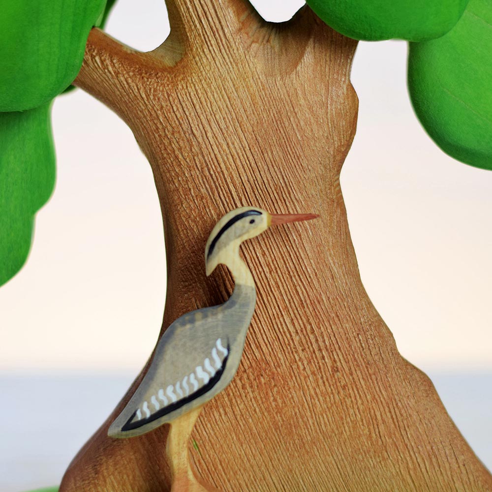 Close up of a handmade wooden Bumbu bird in front of the large green wooden Bumbu oak tree