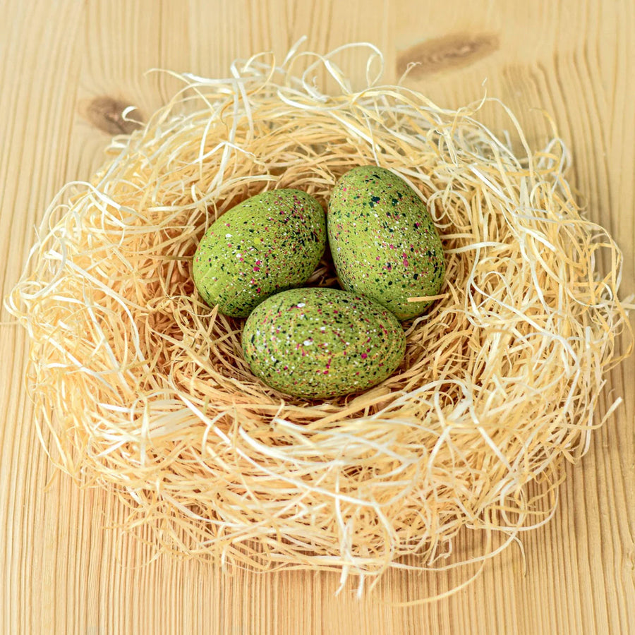 A birds-eye view of the Bumbu Wooden T-Rex Eggs Set. Three speckled green dinosaur eggs sat in a nest