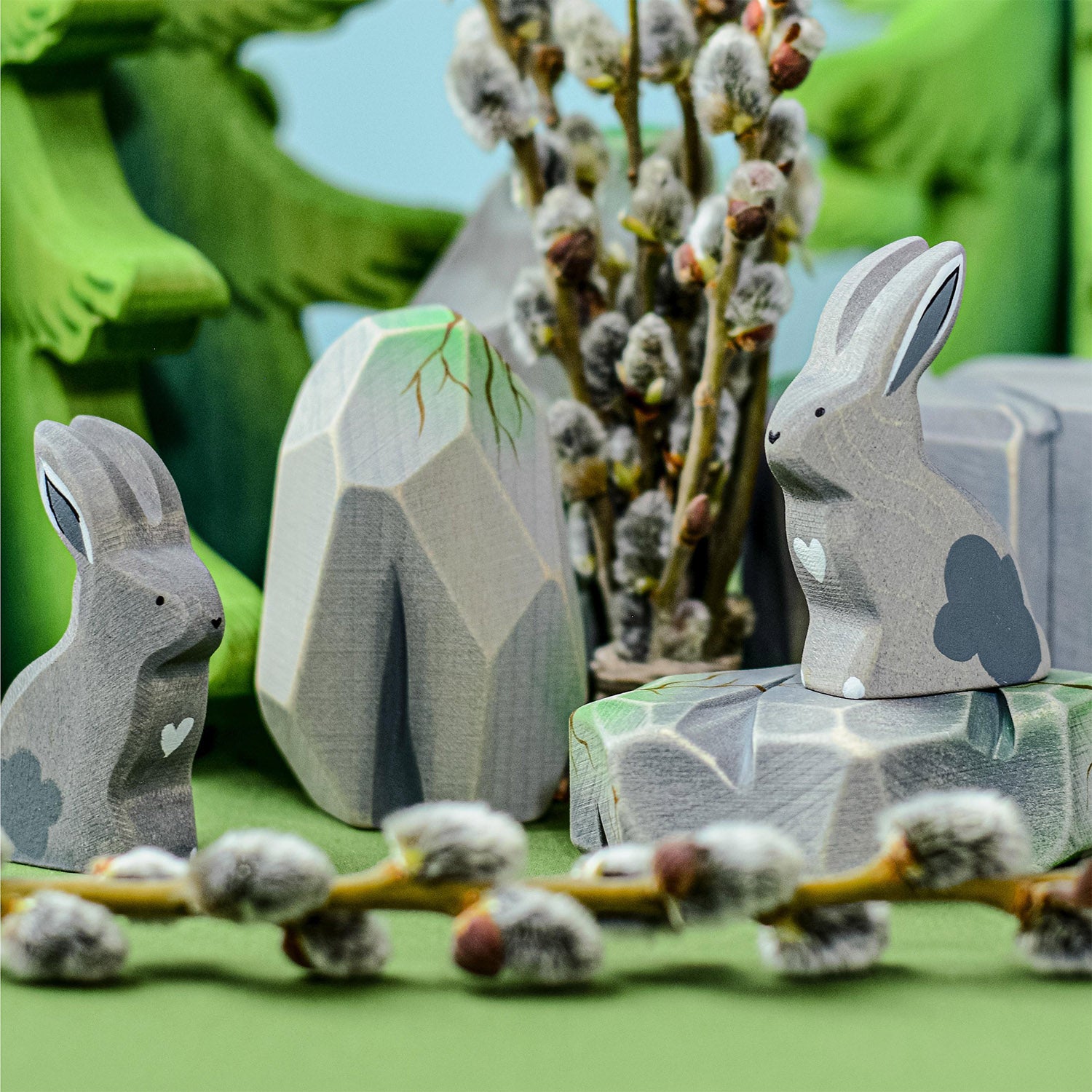 Bumbu Wooden Grey Sitting Rabbit. There are two grey rabbits sitting amongst wooden rocks and trees.