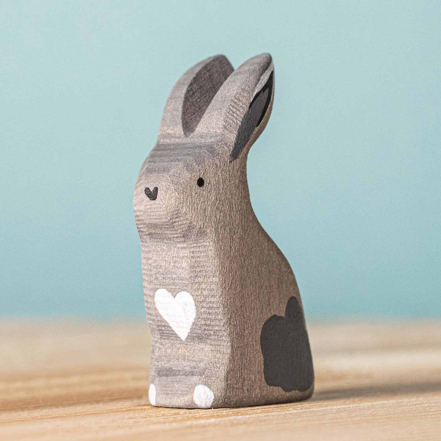 Bumbu Wooden Grey Sitting Rabbit. The toy sits on a wooden surface against a blue background.