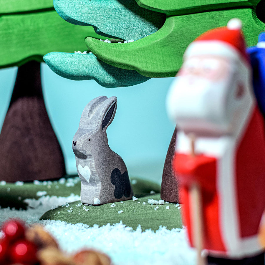 Bumbu Wooden Grey Sitting Rabbit. The toy sits in a festive setting with snow around.