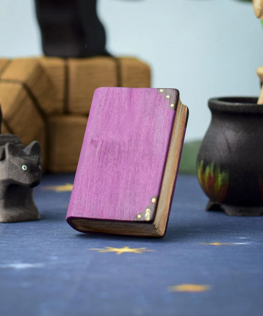 A Bumbu Toys Large purple Book shown at the centre of a Halloween themed play scene. Other Halloween themed wooden toys can be seen in the background. 