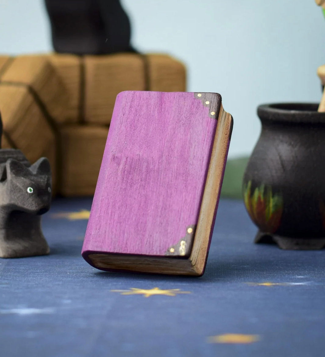 A Bumbu Toys Large purple Book shown at the centre of a Halloween themed play scene. Other Halloween themed wooden toys can be seen in the background. 