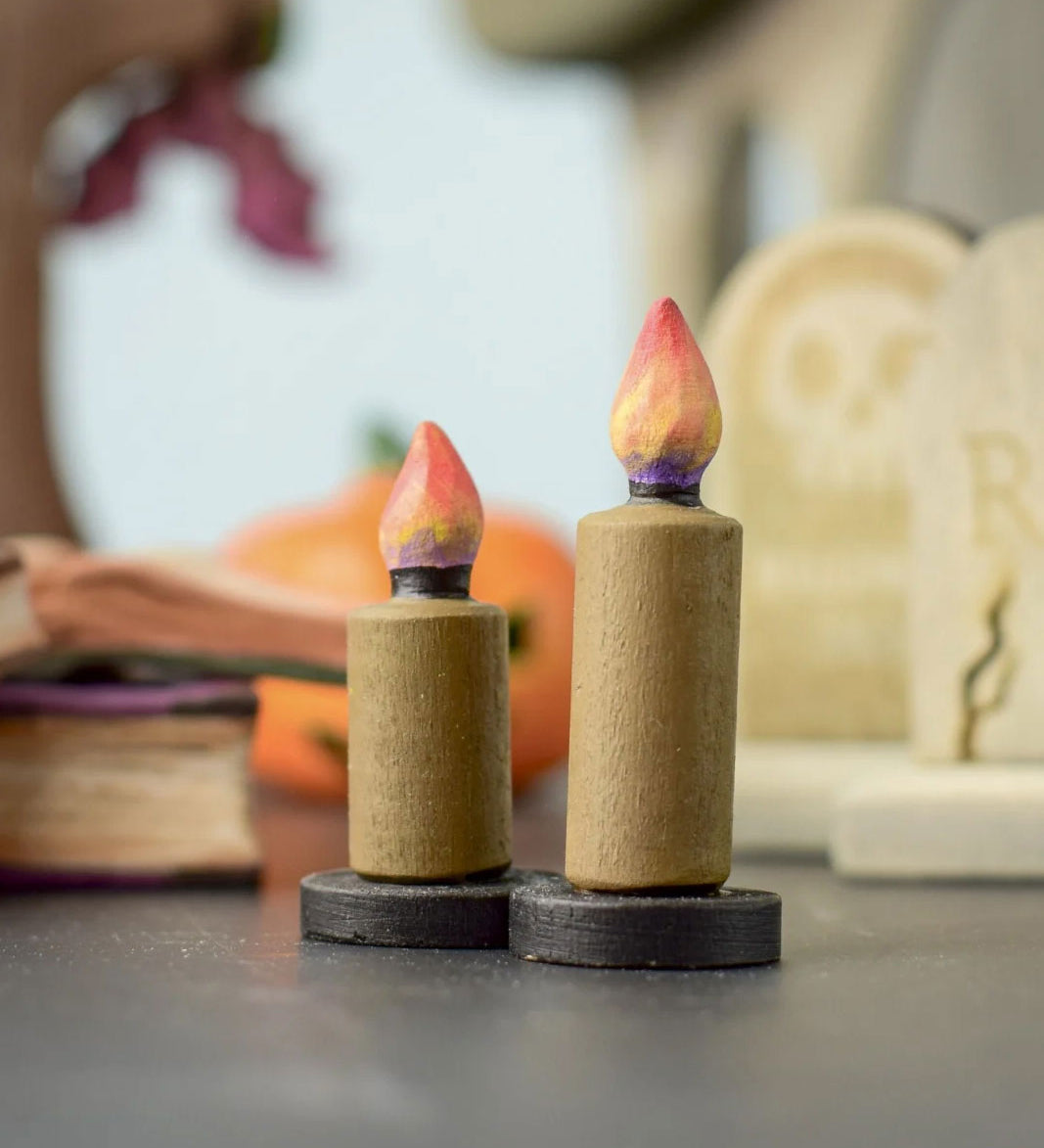 Bumbu Toys wooden Candle figures Set. The candles have a beige colour, on a black coloured base with a flame on the top. One candle is taller than the other. The candles are placed at the front and centre of a Halloween themed small world play set up. 