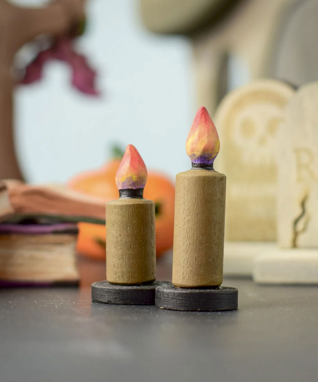 Bumbu Toys wooden Candle figures Set. The candles have a beige colour, on a black coloured base with a flame on the top. One candle is taller than the other. The candles are placed at the front and centre of a Halloween themed small world play set up. 