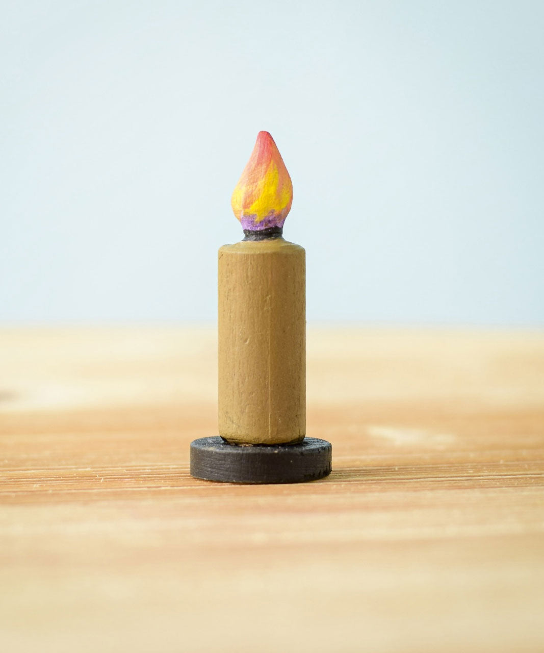 A single candle from the Bumbu Toys wooden Candle figures Set. The candle has been placed on a wooden surface. 