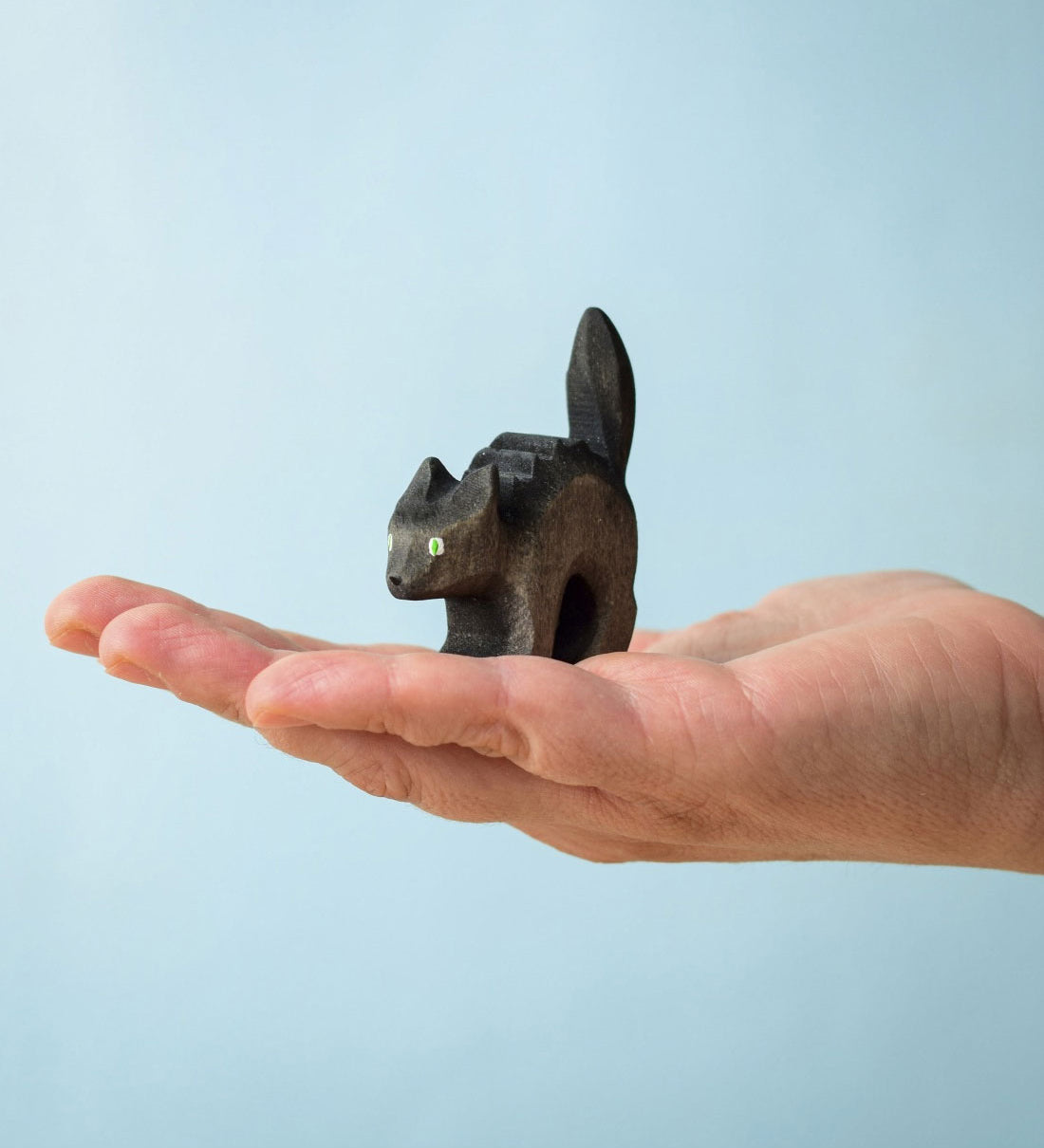 Bumbu Toys Scared Black Cat figure. The cat's tail is stood up and the cat has green eyes. The cat is balanced on a palm of an adult's hand. 