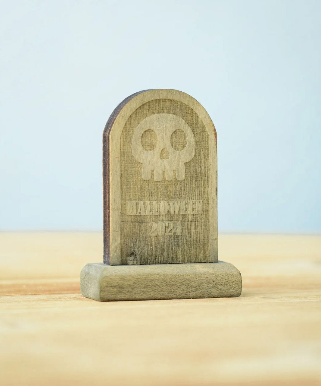 The skull decorated headstone from the Bumbu Toys Gravestones Set. The headstone is placed on a wooden surface.