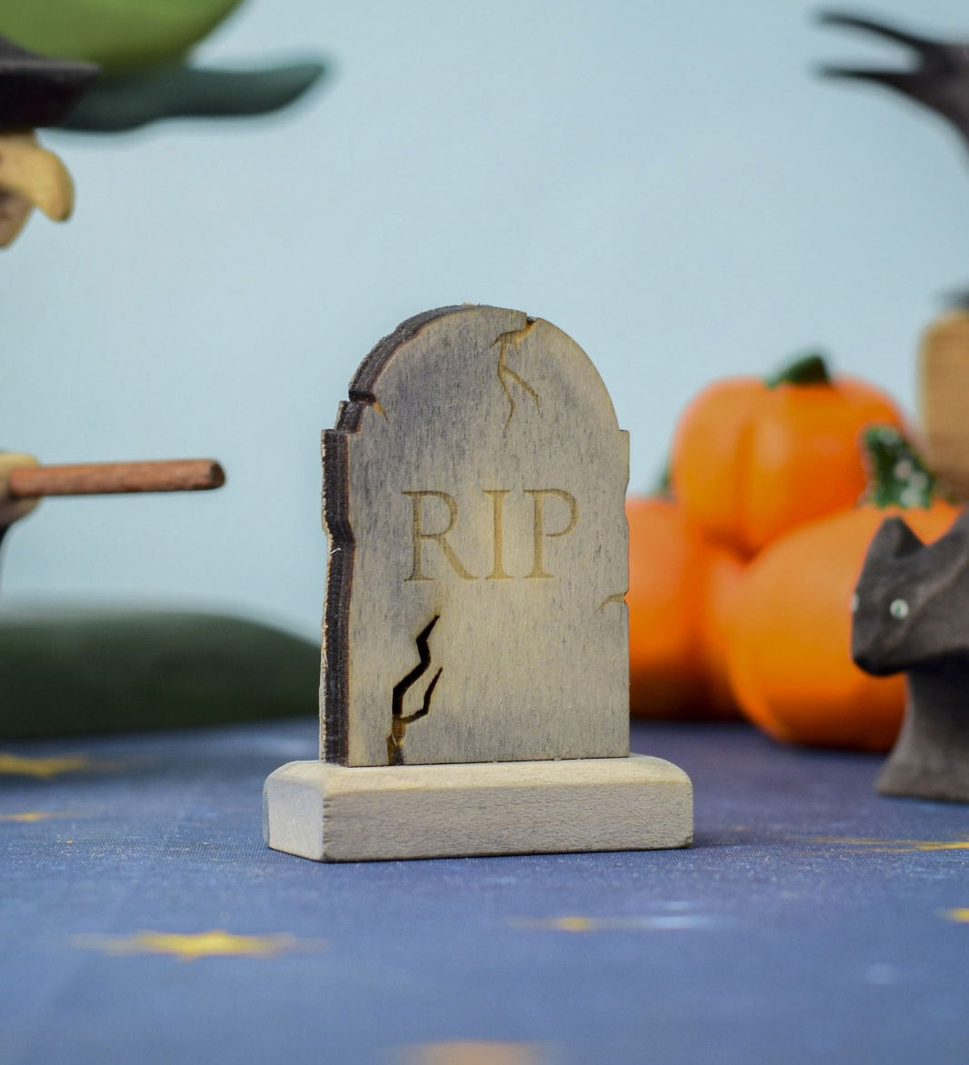 The RIP decorated headstone from the Bumbu Toys Gravestones Set, the gravestone has crack detailing on the edges giving it a spooky Halloween vibe. The headstone is pictured in a Halloween themed play scene. 