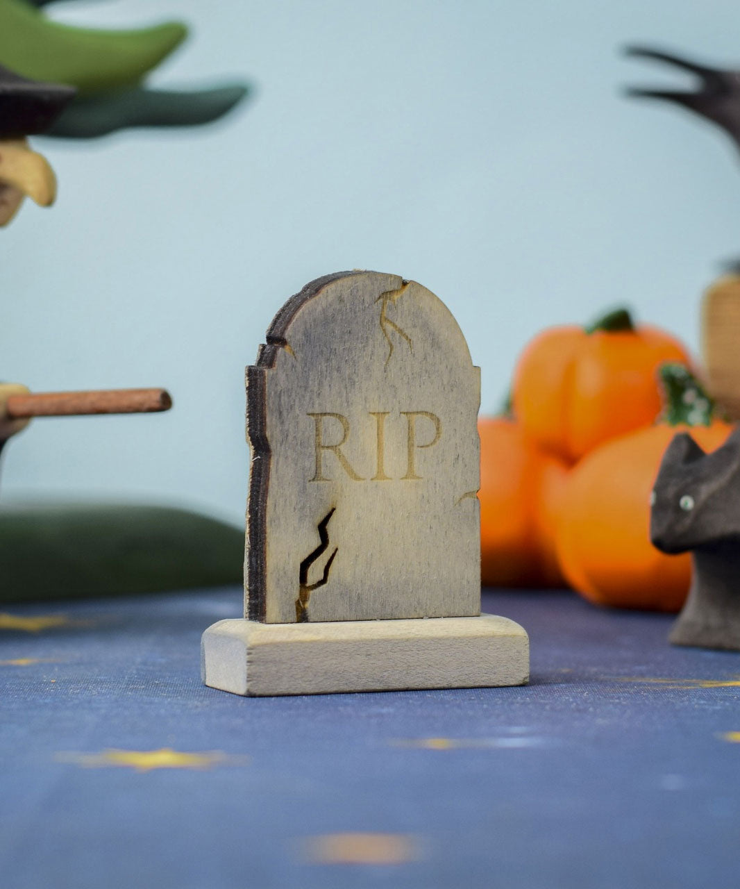 The RIP decorated headstone from the Bumbu Toys Gravestones Set, the gravestone has crack detailing on the edges giving it a spooky Halloween vibe. The headstone is pictured in a Halloween themed play scene. 