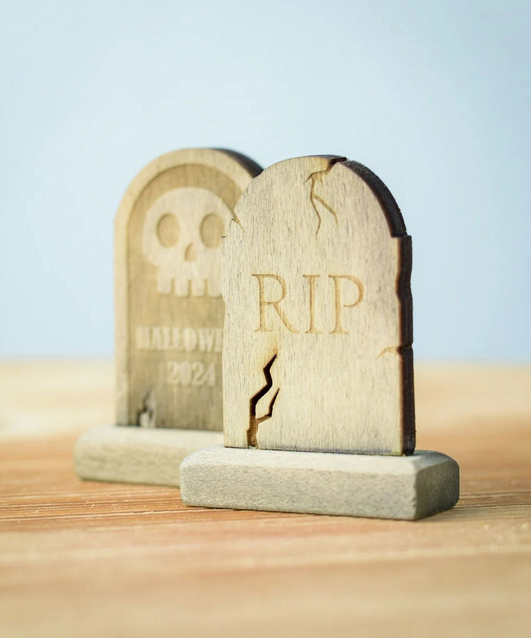 Bumbu Toys Gravestones Set. The set contains two headstones, one is decorated with RIP in large letters the other had a skull with Halloween 2024 written underneath. The Headstones are placed on a wooden surface.