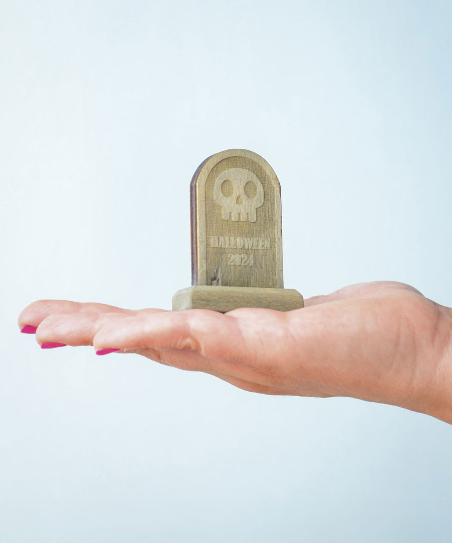 The skull decorated headstone from the Bumbu Toys Gravestones Set. The headstone is placed on an adult's hand.