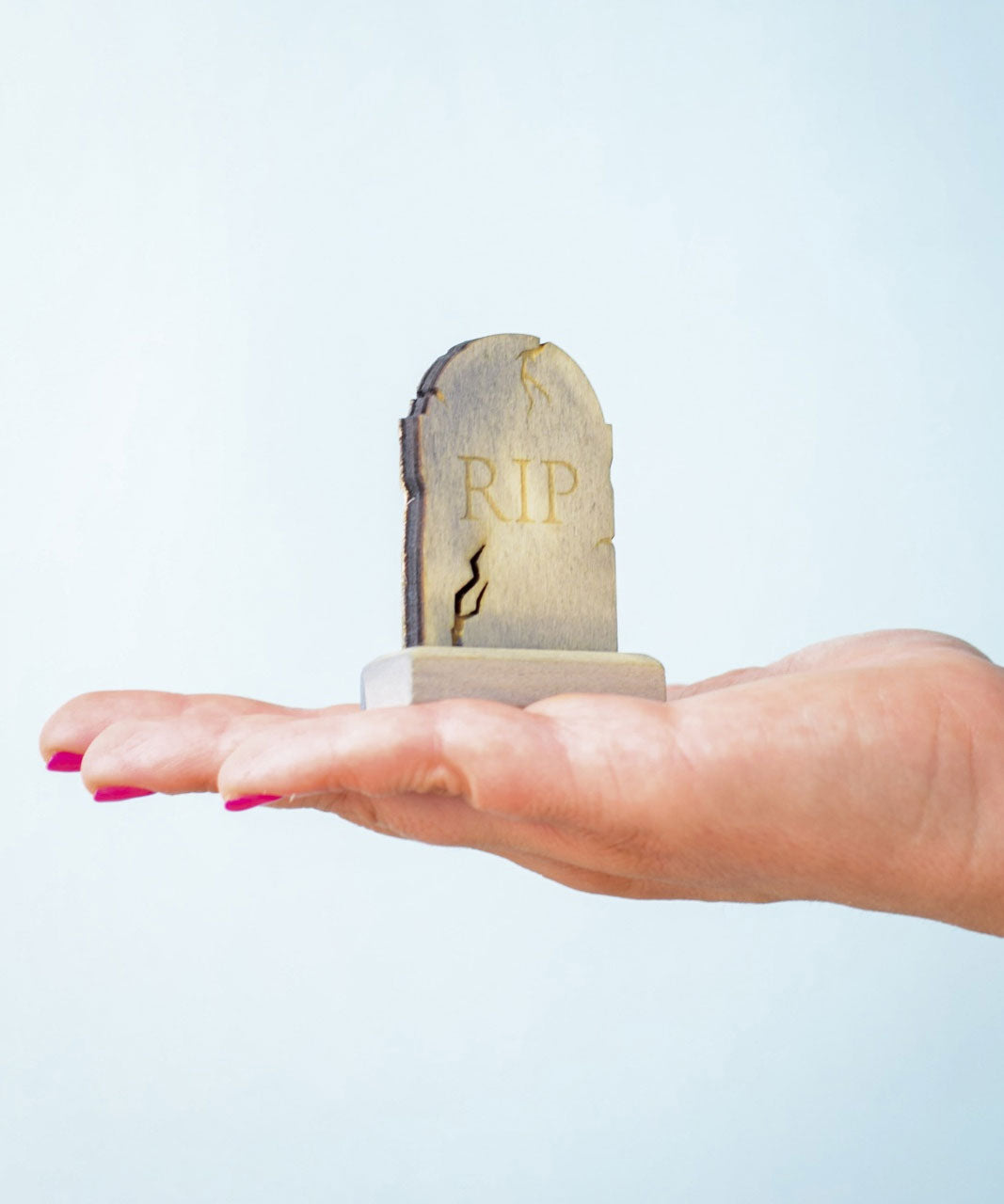 The RIP decorated headstone from the Bumbu Toys Gravestones Set. The headstone is placed on an adult's hand.