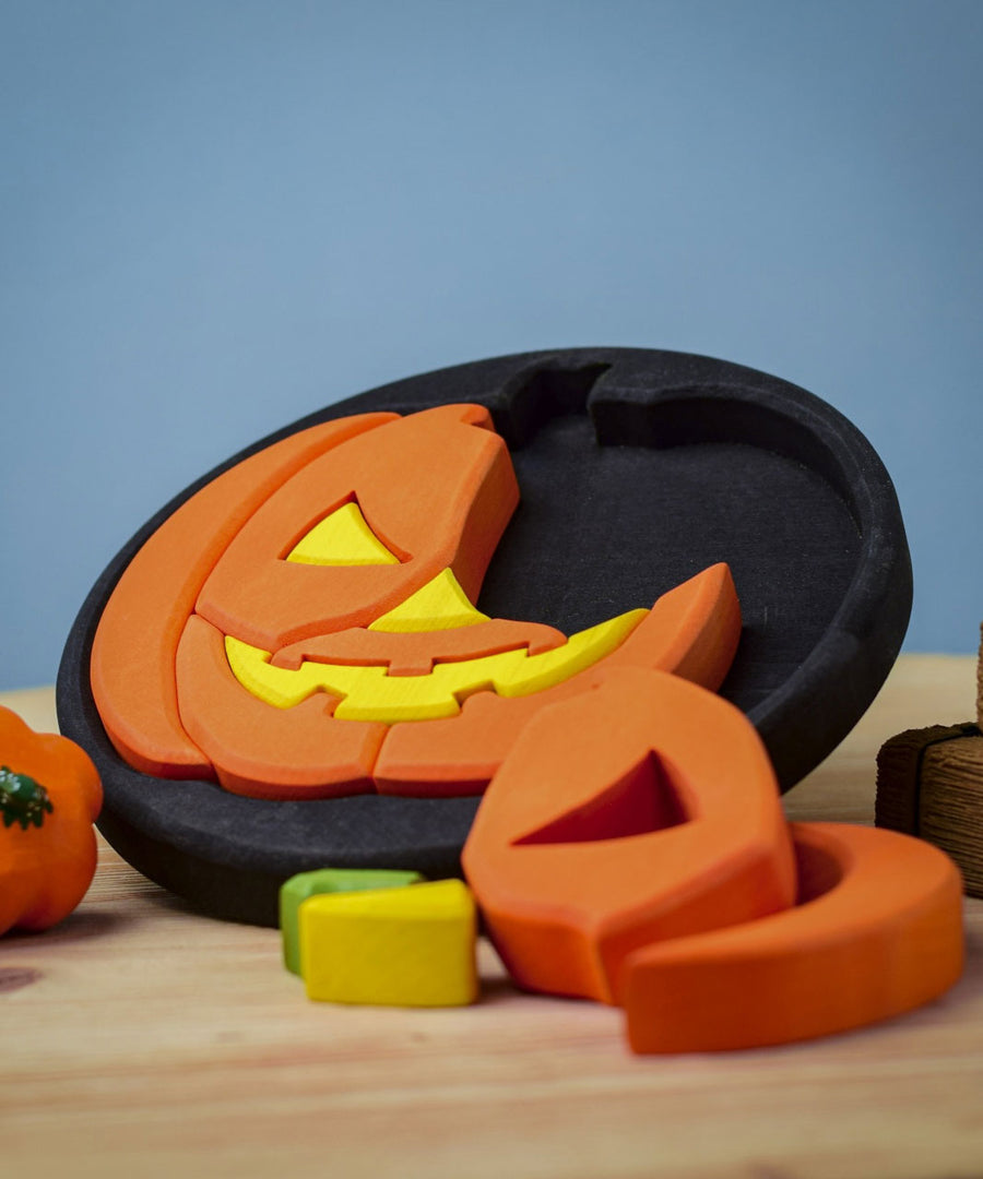 The Bumbu Halloween Pumpkin Round Wooden Puzzle pictured on it's black coloured base frame. The puzzle is propped up on it's side on a wooden surface.