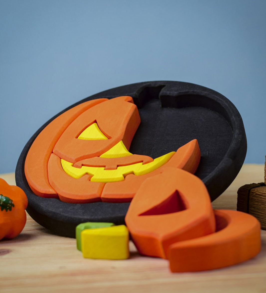 The Bumbu Halloween Pumpkin Round Wooden Puzzle pictured on it's black coloured base frame. The puzzle is propped up on it's side on a wooden surface.