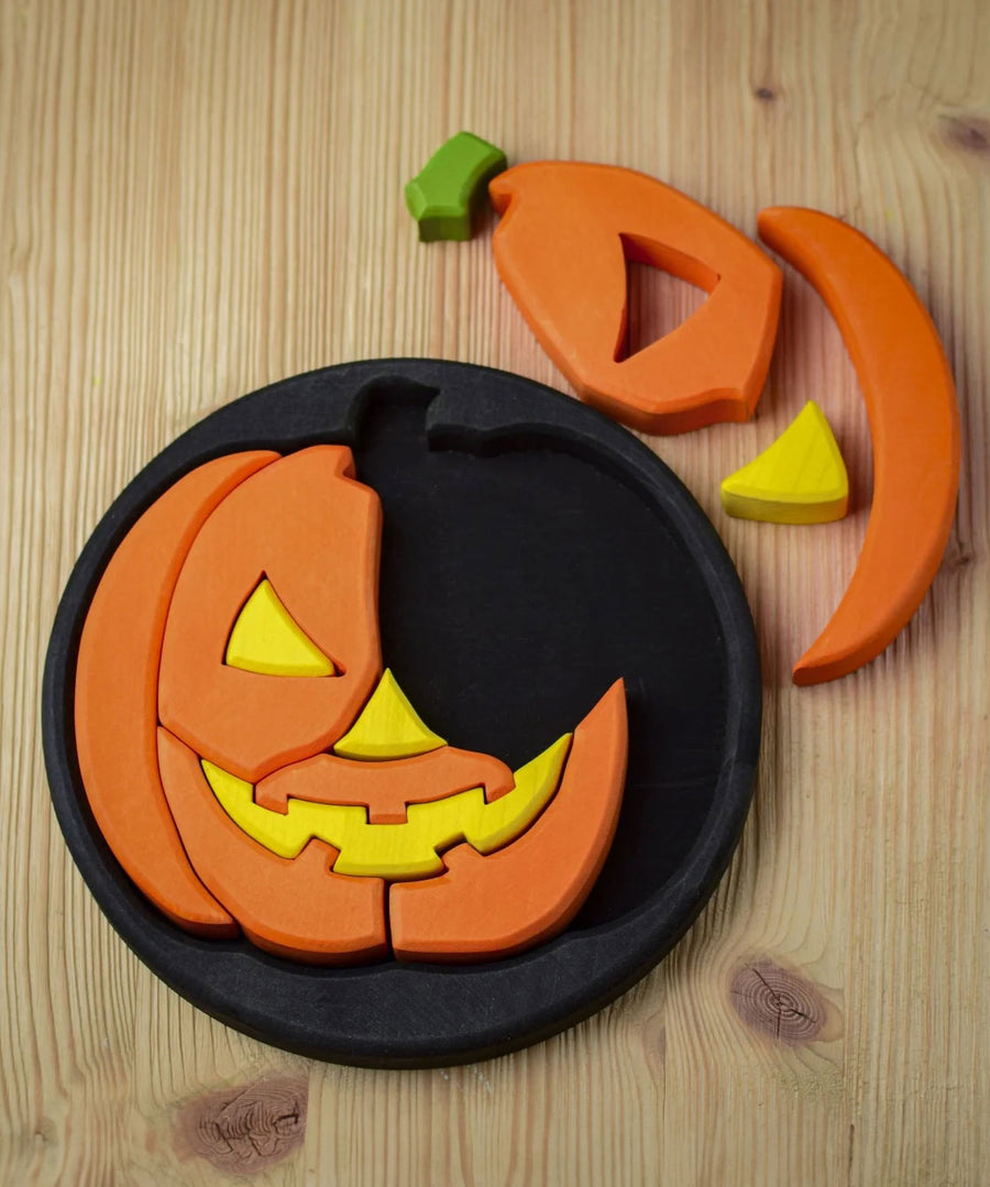 The Bumbu Halloween Pumpkin Round Wooden Puzzle pictured on it's black coloured base frame with 4 of the pieces taken out. The puzzle is pictured from above on a wooden surface.