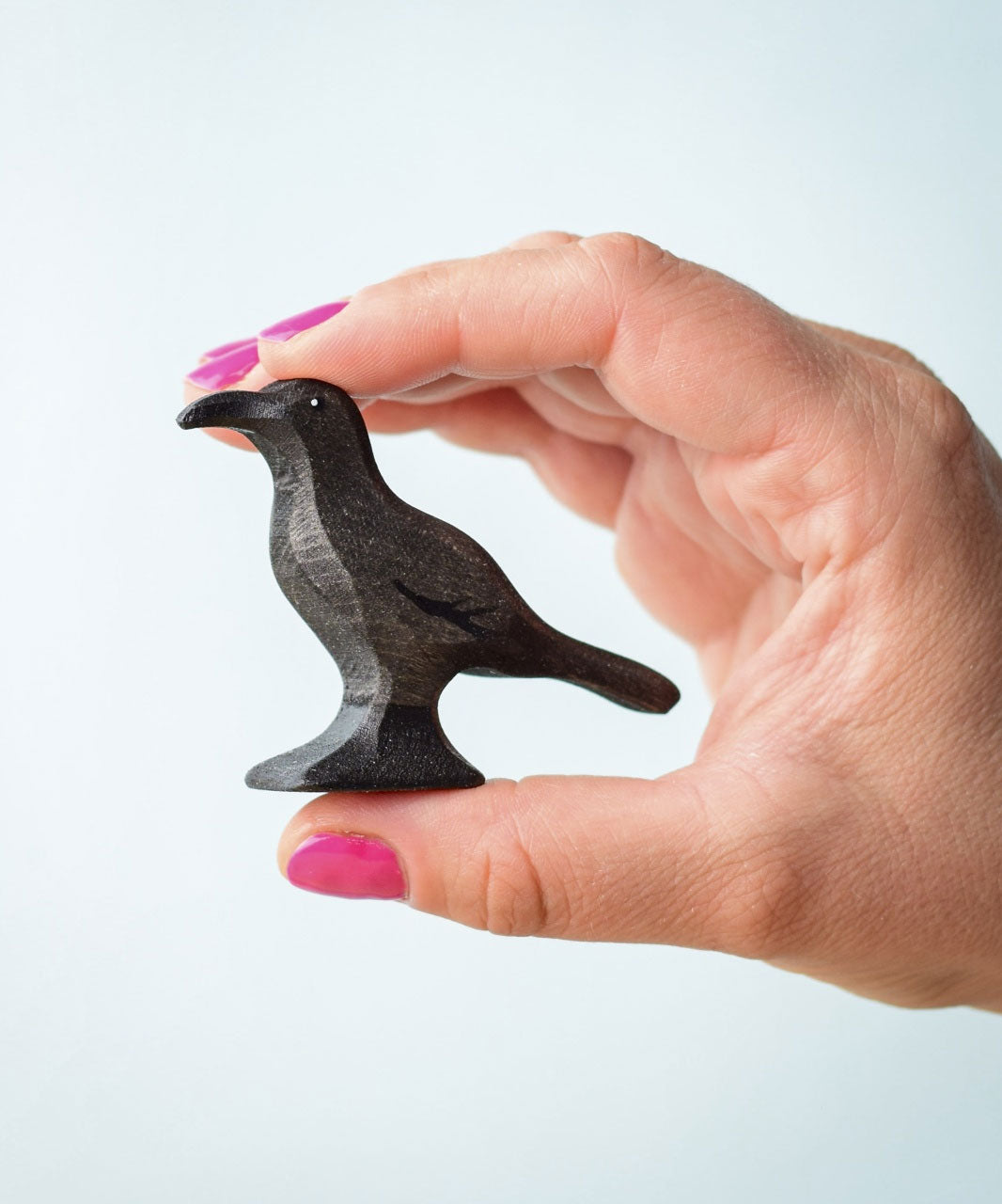 Bumbu Toys wooden Raven figure being held in an adult's hand. The person has bright pink nail polish.