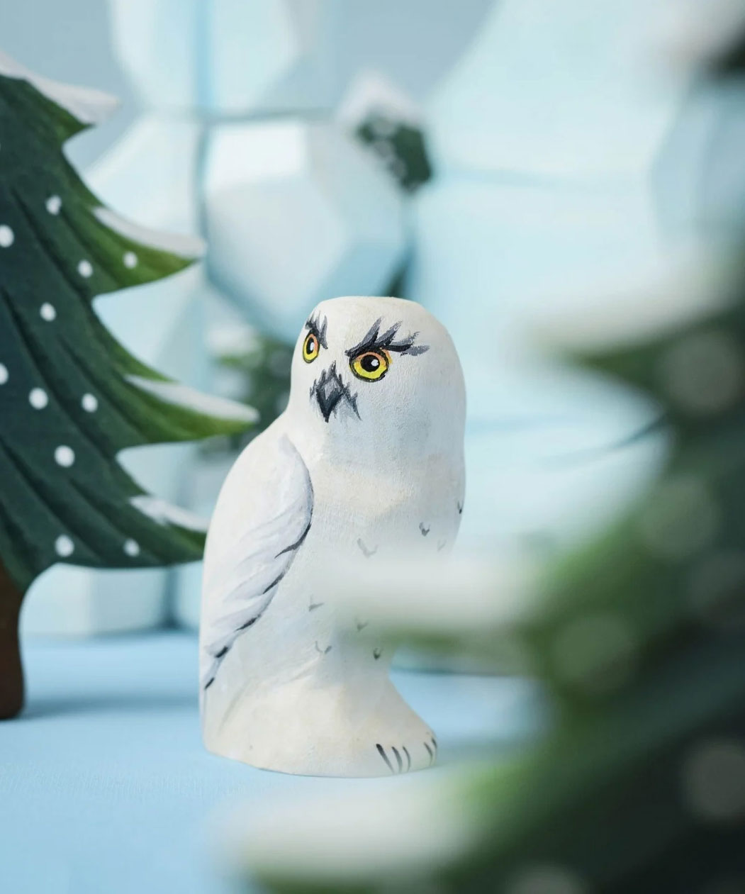 A close up of the Bumbu Toys Snowy Owl in a small world play scene. Other Bumbu toys can be seen blurred in the background.