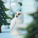 A close up of the Bumbu Toys Snowy Owl in a small world play scene. Other Bumbu toys can be seen blurred in the background.