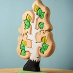 The Bumbu Toys Big Puzzle Birch Tree showing the green leaves side placed on a wooden surface in front of a blue background.