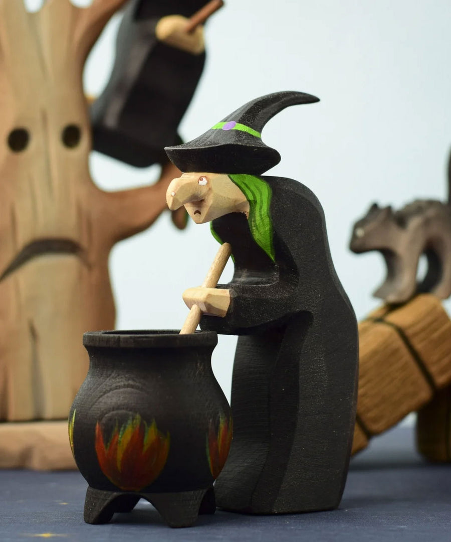 A Bumbu Toys brewing witch figure standing in front of a Bumbu Cauldron in a spooky Halloween themed play scene. 