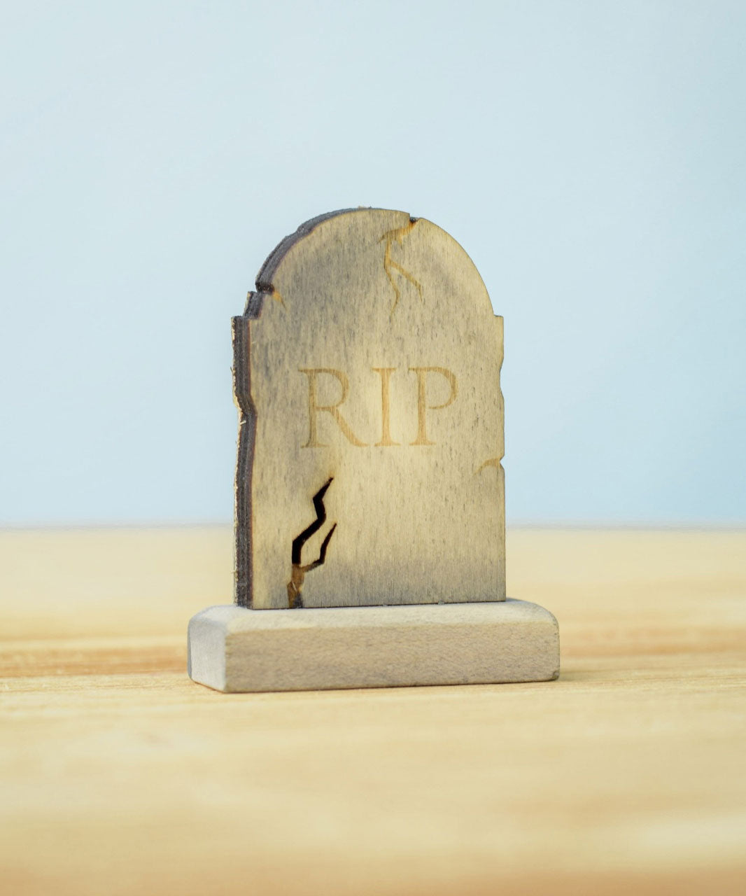 The RIP decorated headstone from the Bumbu Toys Gravestones Set. The headstone is placed on a wooden surface.