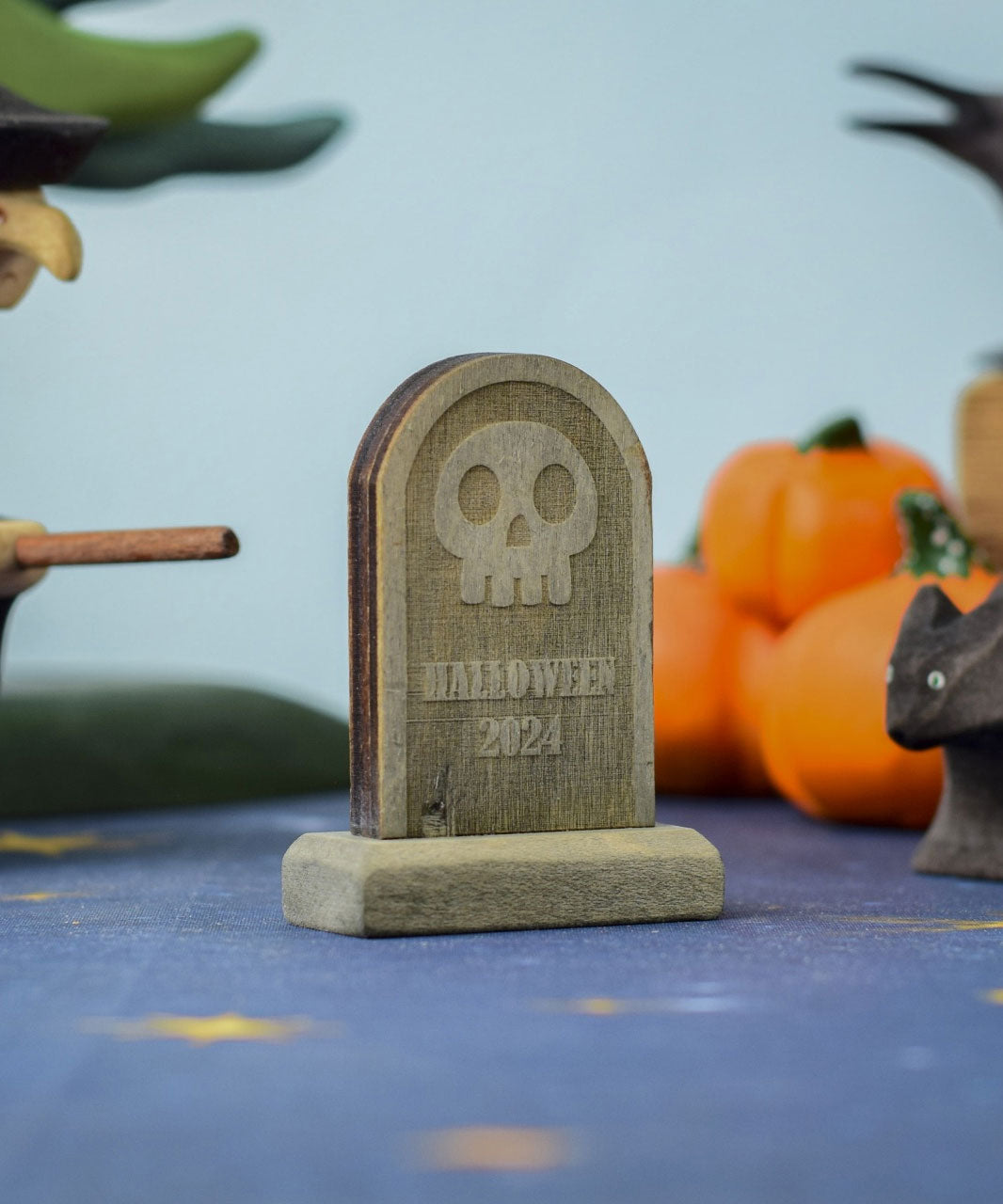 The skull decorated headstone from the Bumbu Toys Gravestones Set. The headstone is pictured in a Halloween themed play scene. 