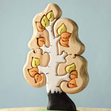 The Bumbu Toys Big Puzzle Birch Tree showing the orange and yellow leaves side, placed on a wooden surface in front of a blue background.