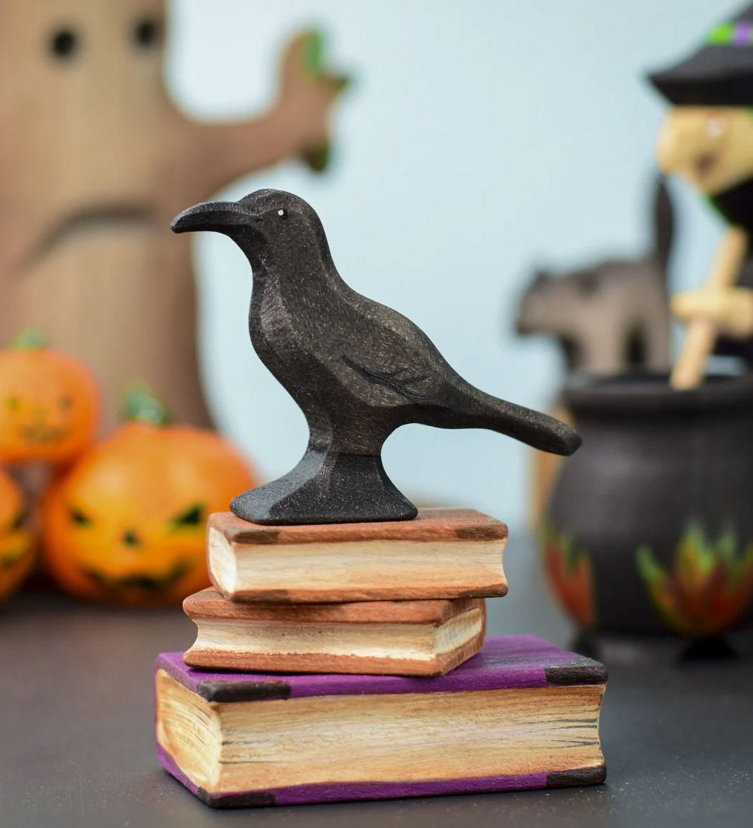 The Bumbu Toys Raven placed on a pile of wooden Bumbu books at the front and centre of a Halloween themed small world play set up. 