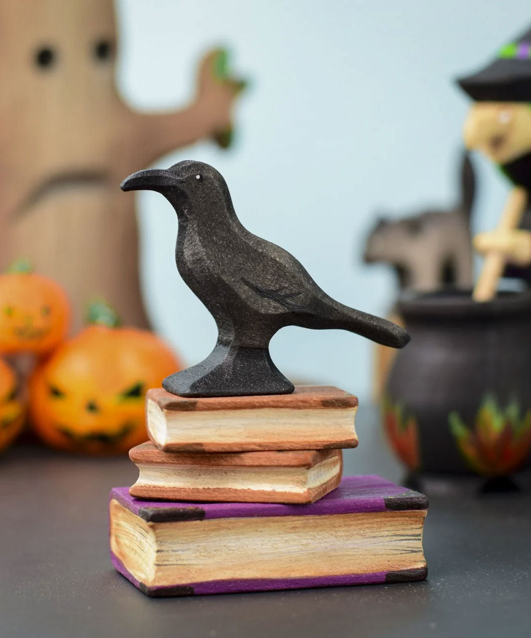 The Bumbu Toys Raven placed on a pile of wooden Bumbu books at the front and centre of a Halloween themed small world play set up. 