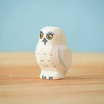 The Bumbu Toys Snowy Owl Chick placed on a wooden surface in front of a blue coloured background. 