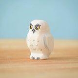 The Bumbu Toys Snowy Owl Chick placed on a wooden surface in front of a blue coloured background. 