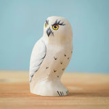 The Bumbu Toys Snowy Owl wooden toy figure placed on a wooden surface in front of a blue background.