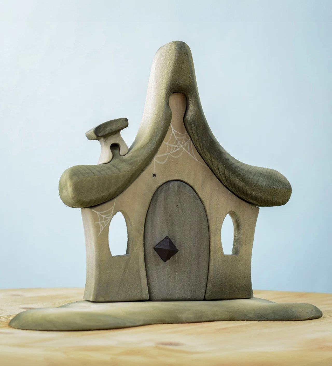 Bumbu Toys Witches house decorated with a Halloween theme. The house is grey in colour hand has cobwebs and a spider painted on. The House is placed on a wooden surface.