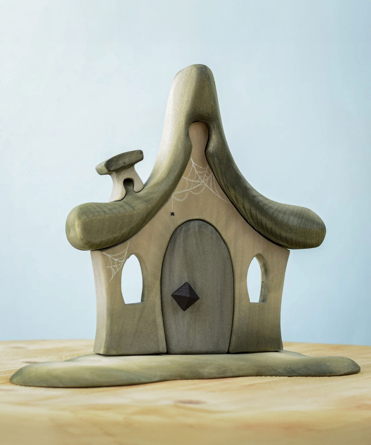 Bumbu Toys Witches house decorated with a Halloween theme. The house is grey in colour hand has cobwebs and a spider painted on. The House is placed on a wooden surface.